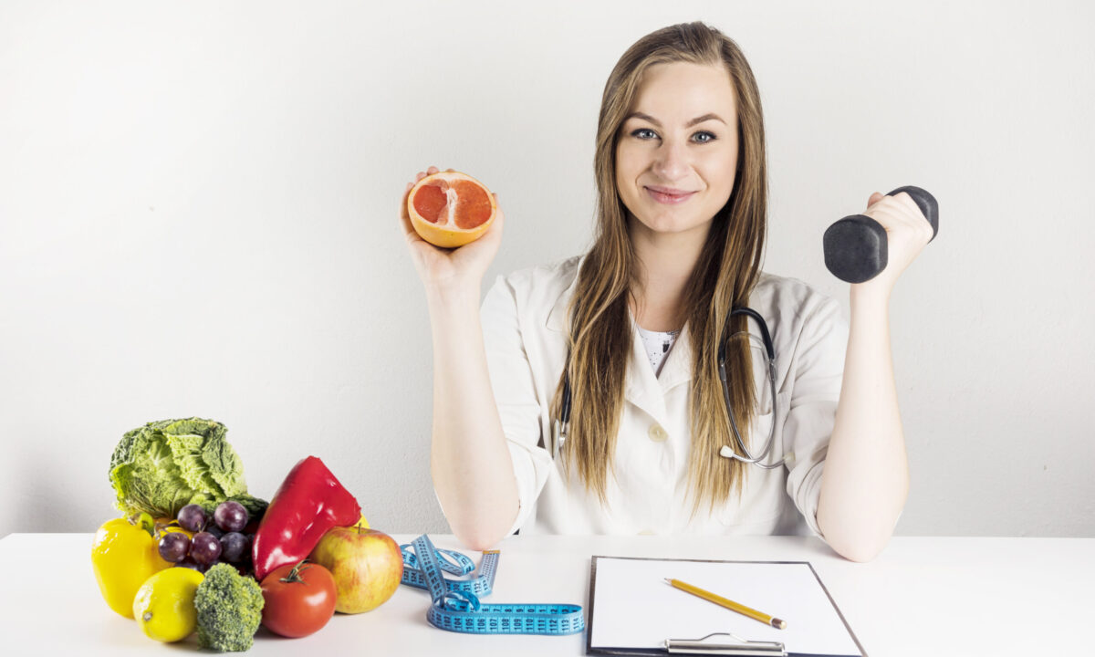 female-dietician-holding-grapefruit-dumbbell-clinic